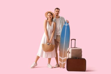 Güzel, genç, mutlu, bavullu ve pembe arka planda sörf tahtası olan bir çift turist.