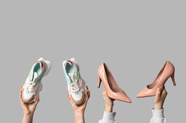 Tarz sahibi spor ayakkabılı kadın elleri ve gri arka planda yüksek topuklu bej ayakkabılar.