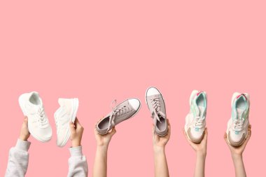 Pembe arka planda farklı şık spor ayakkabıları olan kadın elleri.