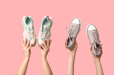 Pembe arka planda farklı şık spor ayakkabıları olan kadın elleri.