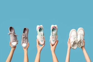 Mavi arka planda farklı şık spor ayakkabıları olan kadın elleri.