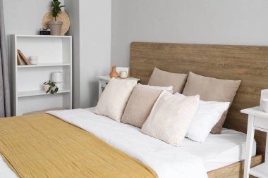 Büyük yataklı, yastıklı, raf üniteli ve komodinli modern yatak odası.