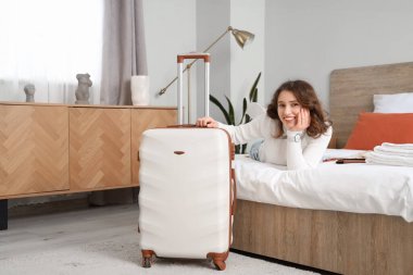 Otel odasında bavullu bir kadın turist yatağında yatıyor.