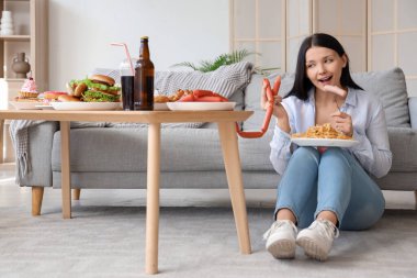 Evde sosis ve makarna olan genç bir kadın. Aşırı yeme kavramı