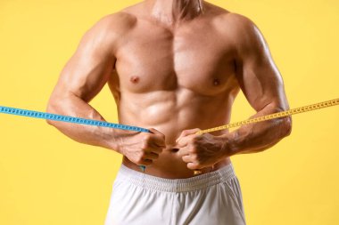 Sarı arka planda mezuraları olan erkek vücut geliştirici, yakın plan.