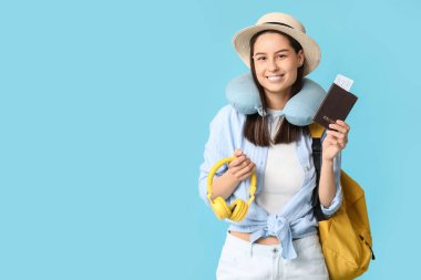 Şapkalı, şapkalı, kulaklık takan ve mavi arka planda sırt çantası olan genç bir kadın. Seyahat kavramı