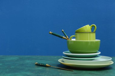 Masada mavi arkaplana karşı yeşil, temiz sofra takımı ve çatal bıçak yığını
