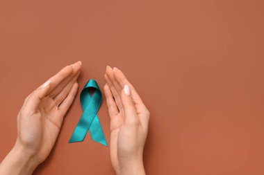 Kahverengi arka planda deniz mavisi kurdeleli kadın elleri. Cinsel Saldırı Bilinci Ayı