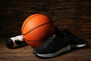 Siyah spor ayakkabıları, basketbol ve spor şişeleri ahşap arka planda.