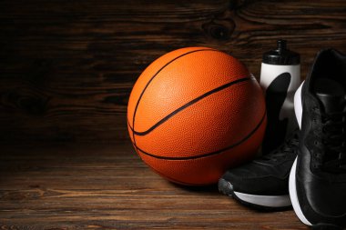 Siyah spor ayakkabıları, basketbol ve spor şişeleri ahşap arka planda.