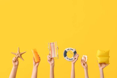 Güneş kremi, denizyıldızı, minyatür iskemle, dekoratif can simidi, deniz kabuğu ve sarı arka planda yüzme kolu olan kadın elleri. Seyahat kavramı.