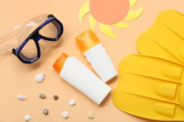 Güneş kremi şişeleri, dalış maskesi ve turuncu arka planda paletler.