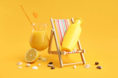 Bir şişe güneş kremi ve arka planda bir bardak meyve suyu olan iskemle.