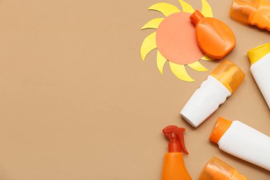 Güneş kremi şişeleri ve kahverengi arka planda kağıt güneş figürü