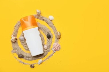 Sarı arka planda bir şişe güneş kremi, kum ve deniz kabuğu.