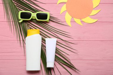 Güneş gözlüğü, şişe ve güneş koruyucu krem pembe ahşap arka planda.