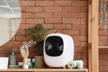 Küçük kozmetik buzdolabı tuğla duvarın yanındaki ahşap çekmecede.