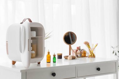 Pencerenin yanındaki masada kozmetik buzdolabı var.