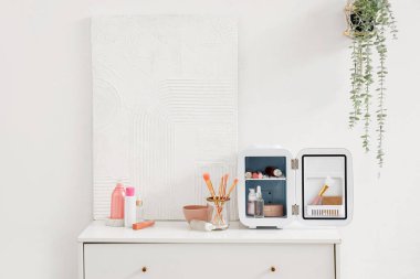 Kozmetik ürünleri olan kozmetik buzdolabı ve beyaz duvarın yanındaki çekmecelerin üzerine resim.