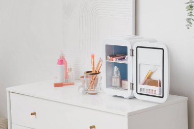 Beyaz duvarın yanındaki çekmecelerde kozmetik ürünleri olan küçük bir buzdolabı.