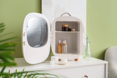 Küçük buzdolabı, kozmetik ürünleri ve yeşil duvarın yanındaki çekmecelerin üzerindeki boya.