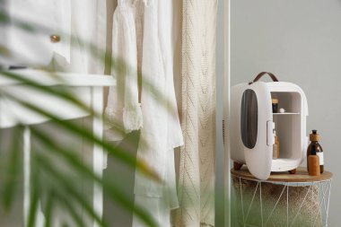 Gri duvarın yanında küçük buzdolabı ve kozmetik ürünleri olan bir masa.