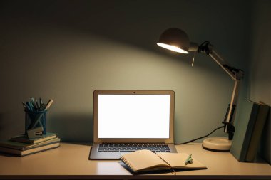 Modern dizüstü bilgisayarı, kırtasiyesi ve yeşil duvarın yanında parlayan lambası olan işyeri