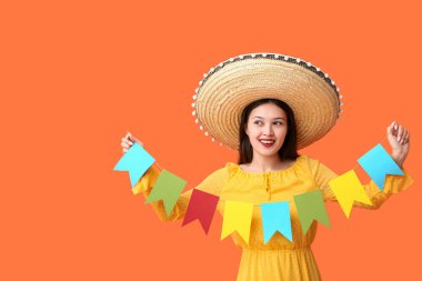 Meksika şapkalı mutlu Asyalı kadın ve turuncu arka planda şenlikli çelenk