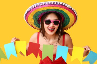 Meksika şapkalı ve sarı arka planda çelengi olan mutlu genç kadın.