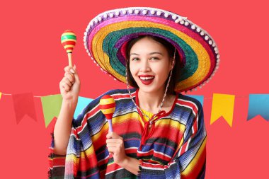 Kırmızı arka planda marakas ve çelenklerle Meksika elbiseli mutlu genç bir kadın.