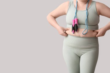 Hafif arka planda ip atlayan şişman bir kadın. Kilo verme konsepti