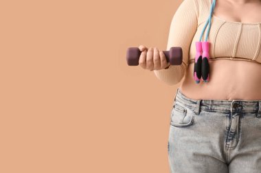 Kilolu, halterli ve bej arka planda ip atlayan bir kadın. Kilo verme konsepti