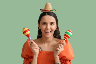 Yeşil arka planda mini şapkası ve marakası olan güzel genç bir kadın.