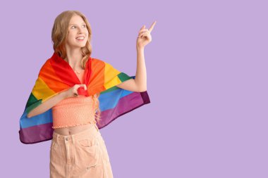 LGBT bayraklı güzel, genç bir kadın mor arka plandaki bir şeyi işaret ediyor.