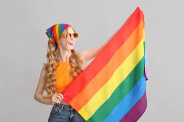 Gri arka planda LGBT bayrağı olan güzel, genç, mutlu bir kadın.