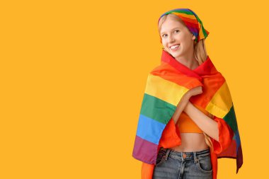 Sarı arka planda LGBT bayrağı olan güzel, genç ve mutlu bir kadın.