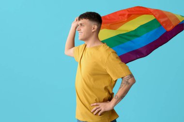 Mavi arka planda LGBT bayrakları olan yakışıklı genç adam.