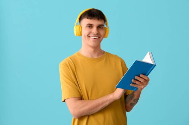 Mavi arka plan kitabı olan kulaklıklı yakışıklı genç adam. Ses kitapçığı kavramı