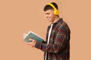 Bej arka plan kitabı olan kulaklıklı yakışıklı genç adam. Ses kitapçığı kavramı