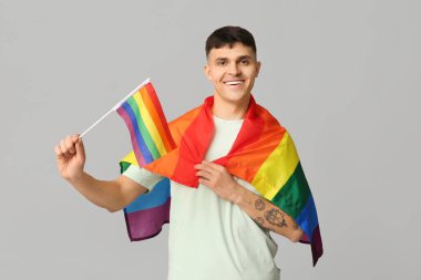 Gri arka planda LGBT bayrakları olan yakışıklı genç adam.