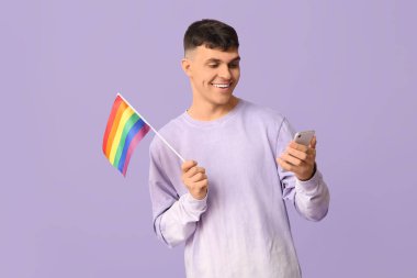 Mor arka planda LGBT bayrağı ve cep telefonu olan yakışıklı genç adam.