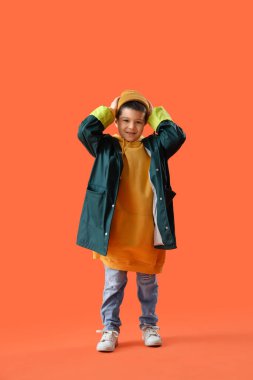 Turuncu arka planda yetişkin kıyafetleri içinde şirin bir Asyalı çocuk.