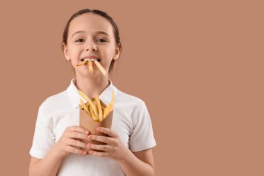 Kahverengi arka planda patates kızartması olan mutlu küçük kız.