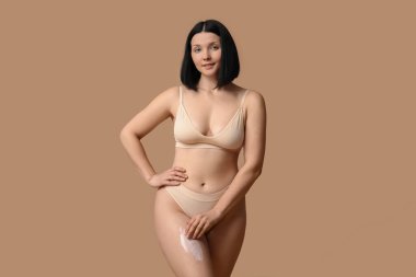 Kahverengi arka planda anti-selülit kremi olan güzel, genç bir kadın.