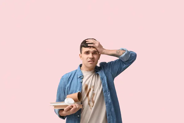 Stressed student in dirty t-shirt with books and paper cup on pink background