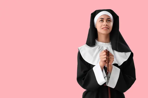 stock image Young nun with beads praying on pink background