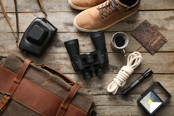 Binoculars, cup of coffee, passport and travel items on wooden background