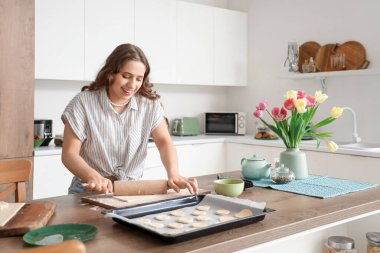 Genç bir kadın mutfaktaki masada kurabiye için para dağıtıyor.