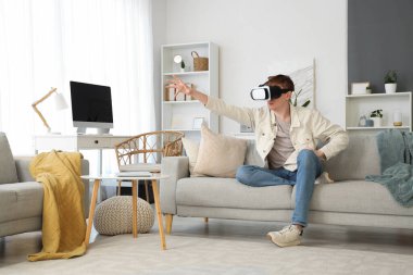 Evdeki kanepede VR gözlük takan genç adam.