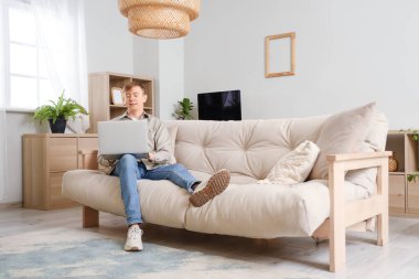 Evdeki kanepede dizüstü bilgisayar kullanan yakışıklı adam.